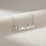Lănțișor argint 925 rodiat cu numele Amalia, pandantiv decupat 38x10 mm font cursiv inițiala A cu buclă jos-stânga, lanț anchor 46 cm pe textil natural ivory tip in cu pliuri