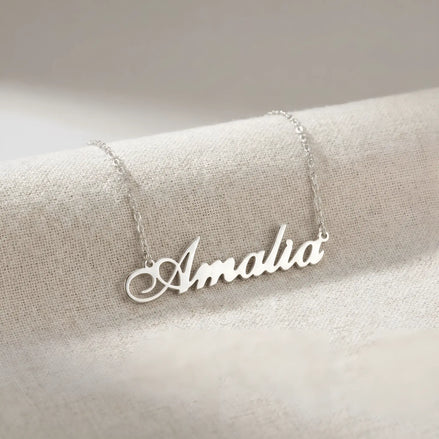 Lănțișor argint 925 rodiat cu numele Amalia, pandantiv decupat 38x10 mm font cursiv inițiala A cu buclă jos-stânga, lanț anchor 46 cm pe textil natural ivory tip in cu pliuri
