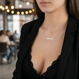 Damă cu păr lung negru purtând lănțișor argint 925 rodiat Amalia pe stern peste top dantelă neagră și sacou negru desfăcut, cafenea cu lumini bokeh