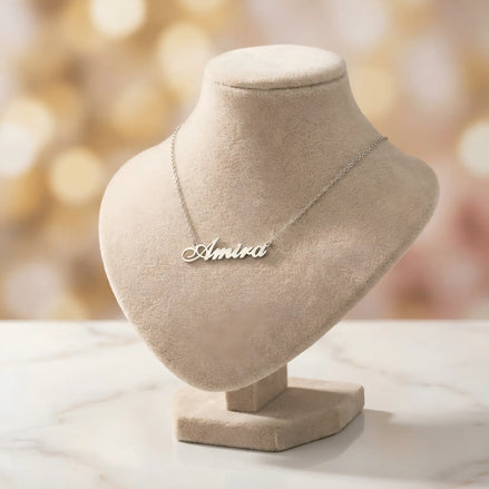 Lănțișor argint 925 rodiat personalizat cu numele Amira decupat în scriere cursivă elegantă cu A și coadă caligrafică pe bust display bej cu lumini bokeh, lanț subțire alb-platinat