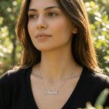 Damă tânără purtând lănțișor argint 925 rodiat cu numele Andra script, peste top negru cu decolteu V, lumină naturală apus în exterior