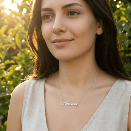 Damă tânără purtând lănțișor argint 925 rodiat cu numele Ariana script, peste top alb de in cu decolteu V, lumină naturală apus în exterior cu vegetație