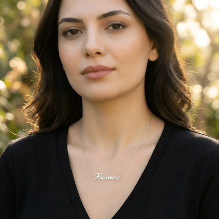 Damă tânără purtând lănțișor argint 925 rodiat cu numele Bianca script, peste top negru cu decolteu V, lumină naturală apus în exterior