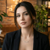 Damă cu păr lung negru prins lejer purtând lănțișor argint 925 rodiat Carina pe stern peste sacou negru desfăcut, cafenea cu cărămidă expusă, lampă industrială și plante