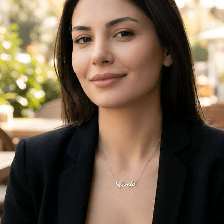 Damă cu păr lung negru purtând lănțișor argint 925 rodiat Carla deasupra claviculei peste sacou negru desfăcut, terasă cu plante lumină naturală caldă