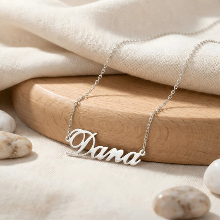 Lănțișor argint 925 rodiat personalizat cu numele Dana decupat în scriere cursivă elegantă cu D mare buclat pe textil alb cu lemn rotund și pietre, lanț subțire alb-platinat