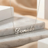 Lănțișor argint 925 rodiat personalizat cu numele Daniela decupat în scriere cursivă elegantă pe marmură bej deschis, lanț subțire alb-platinat