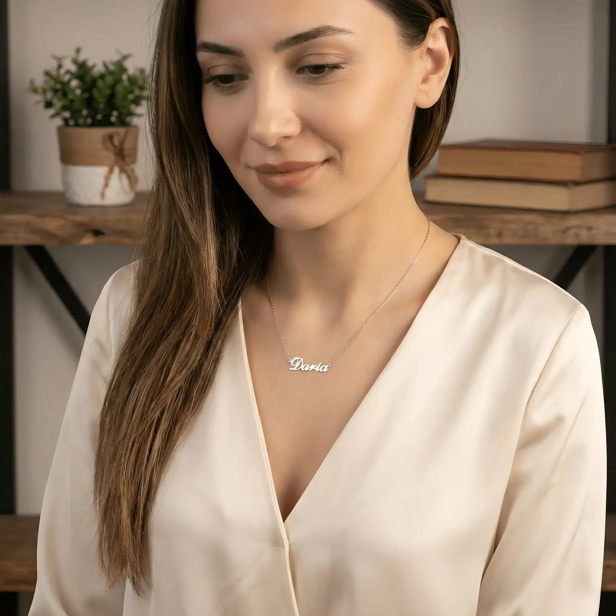 Damă tânără cu păr lung castaniu purtând lănțișor argint 925 rodiat Daria peste bluză satinată ivory cu decolteu V, interior cald cu cărți
