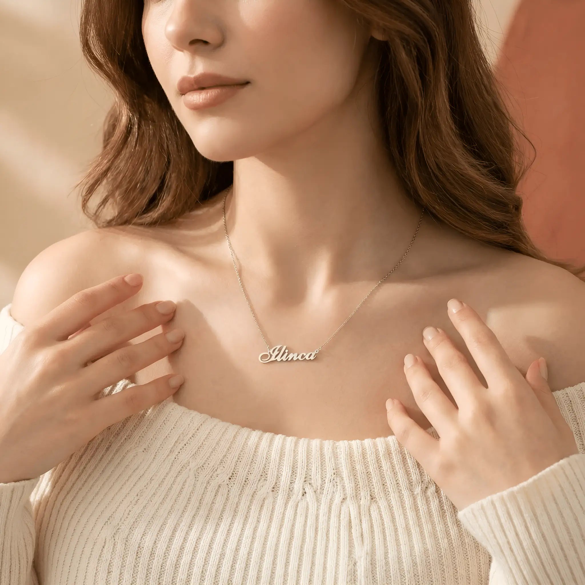 Damă tânără cu păr roșcat purtând lănțișor argint 925 rodiat cu numele Ilinca script, peste pulover crem off-shoulder, lumină caldă interior cu tonuri de toamnă