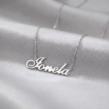 Lănțișor argint 925 rodiat cu numele Ionela, pandantiv decupat 38.5x10 mm font cursiv inițiala I cu coadă subțire descendentă, lanț anchor 46 cm pe textil satinat alb
