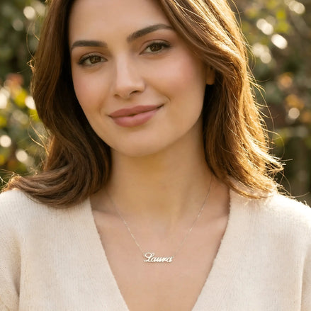 Damă tânără purtând lănțișor argint 925 rodiat cu numele Laura script, peste pulover crem fin de cașmir cu decolteu V, lumină naturală exterior toamnă