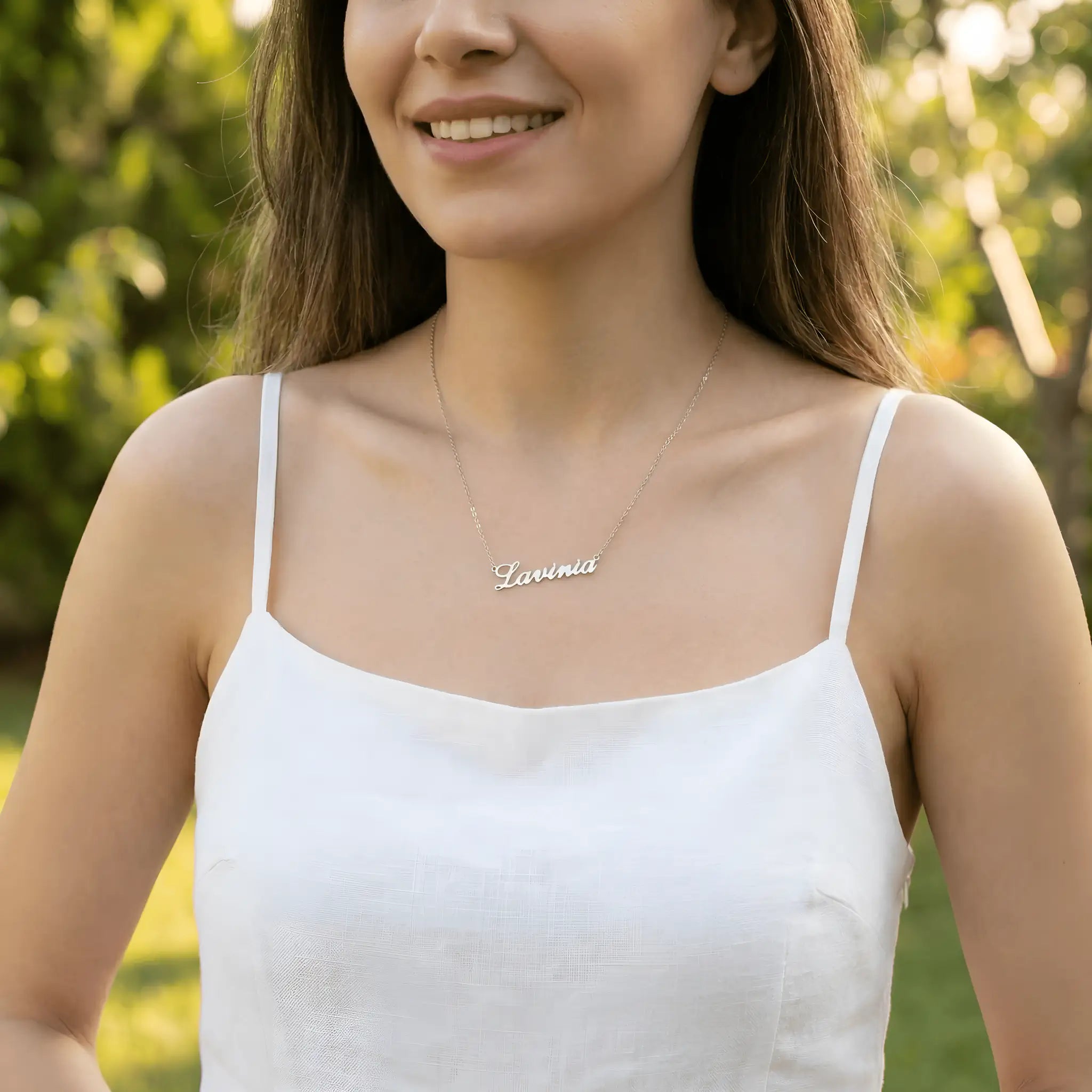 Damă tânără purtând lănțișor argint 925 rodiat cu numele Lavinia script, peste top alb fără bretele de in, lumină naturală exterior cu vegetație de vară