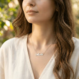 Damă tânără purtând lănțișor argint 925 rodiat cu numele Mada script, peste bluză albă cu decolteu V wrap, lumină naturală exterior cu vegetație