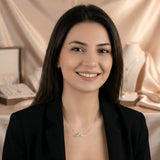 Damă cu păr lung negru purtând lănțișor argint 925 rodiat Mara deasupra claviculei peste sacou negru desfăcut, sală cu draperii satinate ivory și expozitoare de bijuterii
