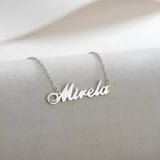 Lănțișor argint 925 rodiat cu numele Mirela, pandantiv decupat 38x10 mm font cursiv inițiala M cu curbă dublă înaltă, lanț anchor 46 cm pe textil natural ivory tip in