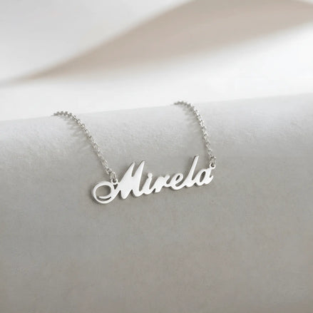 Lănțișor argint 925 rodiat cu numele Mirela, pandantiv decupat 38x10 mm font cursiv inițiala M cu curbă dublă înaltă, lanț anchor 46 cm pe textil natural ivory tip in