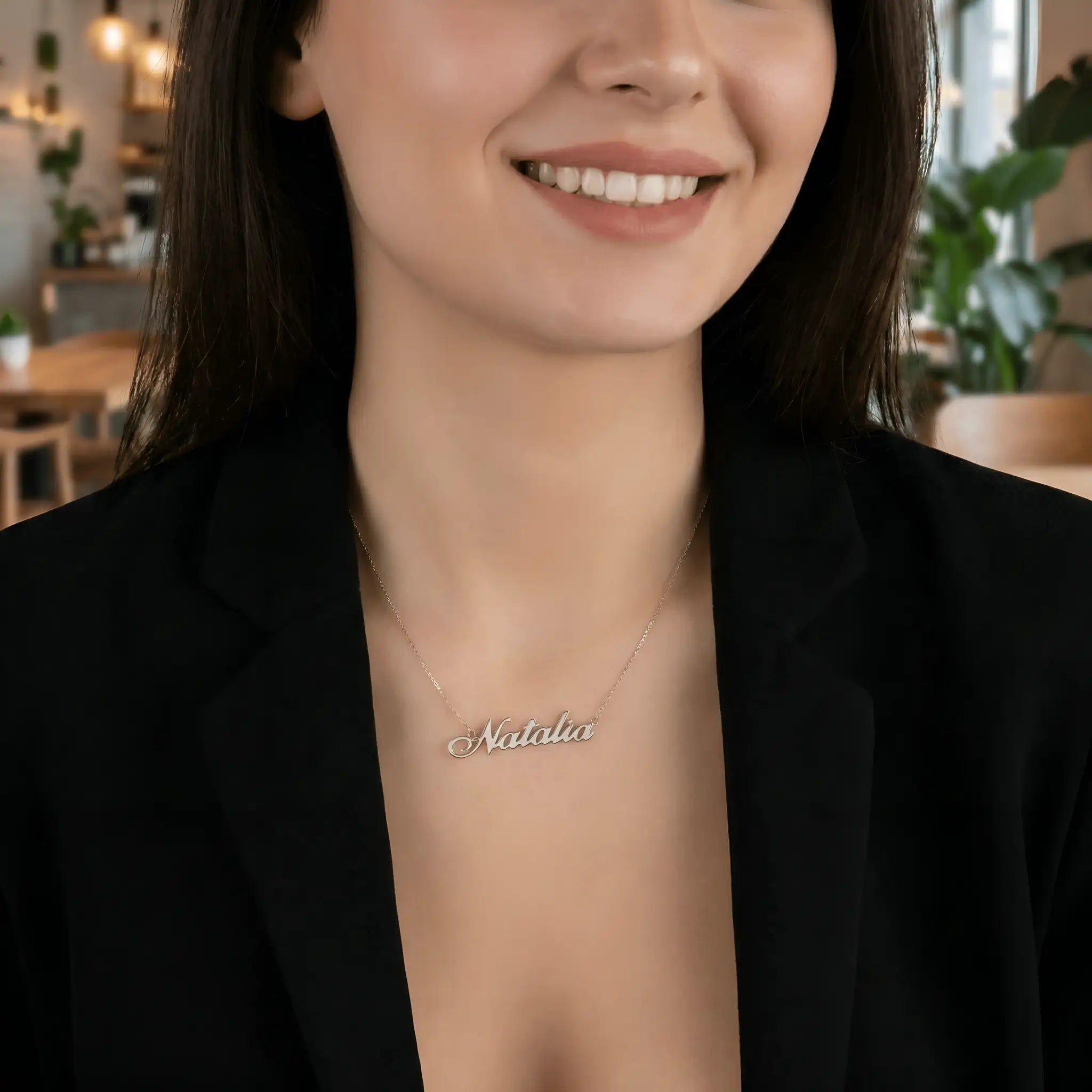 Damă cu păr lung negru bob mediu purtând lănțișor argint 925 rodiat Natalia pe stern peste sacou negru desfăcut, cafenea cu plante și lumini ambient