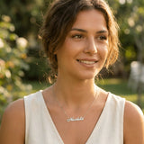 Damă tânără purtând lănțișor argint 925 rodiat cu numele Nicoleta script, peste top alb fără mâneci de in, lumină naturală apus în natură