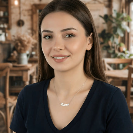 Damă tânără purtând lănțișor argint 925 rodiat cu numele Oana script, peste t-shirt bleumarin cu decolteu V, lumină caldă cafenea rustică cu mobilier de lemn