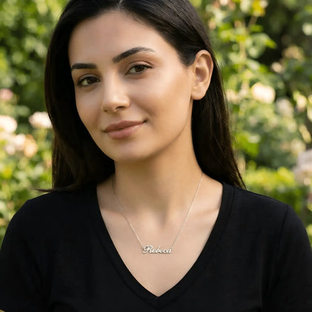 Damă tânără purtând lănțișor argint 925 rodiat cu numele Rebeca script, peste top negru cu decolteu V, lumină naturală exterior cu trandafiri
