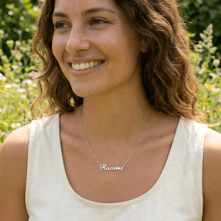Damă tânără purtând lănțișor argint 925 rodiat cu numele Roxana script, peste top alb fără mâneci, lumină naturală exterior cu vegetație
