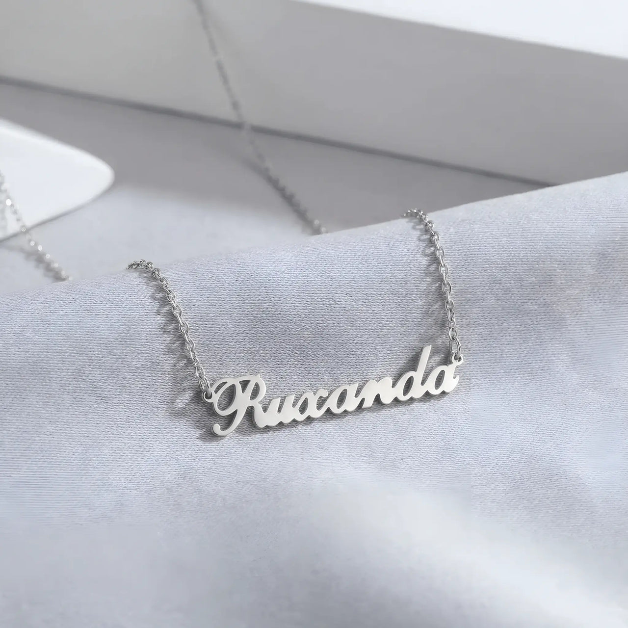 Lănțișor argint 925 rodiat cu nume Ruxanda, caligrafie cursivă decupată pe lanț fin anchor, fundal mătase gri-albastru