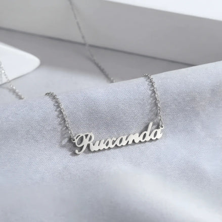 Lănțișor argint 925 rodiat cu nume Ruxanda, caligrafie cursivă decupată pe lanț fin anchor, fundal mătase gri-albastru