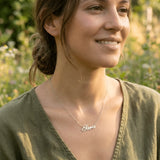 Damă tânără purtând lănțișor argint 925 rodiat cu numele Sara script, peste top de in kaki cu decolteu V, lumină naturală exterior cu wildflowers