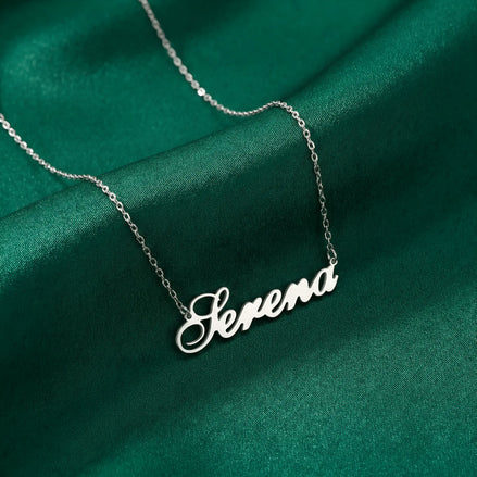 Lănțișor argint 925 rodiat personalizat cu numele Serena decupat în scriere cursivă elegantă cu S ondulat pe drapaj satin verde smarald, lanț subțire alb-platinat