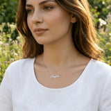 Damă tânără purtând lănțișor argint 925 rodiat cu numele Sofia script, peste t-shirt alb cu decolteu rotund, lumină naturală exterior cu wildflowers