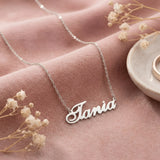 Lănțișor argint 925 rodiat personalizat cu numele Tania decupat în scriere cursivă elegantă cu T cu curbă orizontală pe textil roz cu flori uscate, lanț subțire alb-platinat