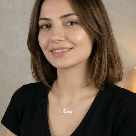 Damă tânără purtând lănțișor argint 925 rodiat cu numele Tania script, peste t-shirt negru cu decolteu V, lumină caldă interior cu lumânare aprinsă
