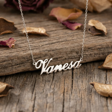 Lănțișor argint 925 rodiat cu numele Vanesa, pandantiv decupat 38.5x10 mm font cursiv, lanț anchor 46 cm pe scândură de lemn vechi cu petale de trandafir uscate