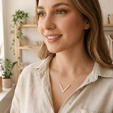 Damă tânără purtând lănțișor argint 925 rodiat cu pandantiv V geometric peste cămașă bej cu decolteu V, dublu V efect editorial, interior cozy cu plante