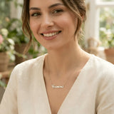 Damă tânără purtând lănțișor argint 925 rodiat cu numele Cosmina script, peste bluză albă de in cu decolteu V, lumină naturală interior cu plante