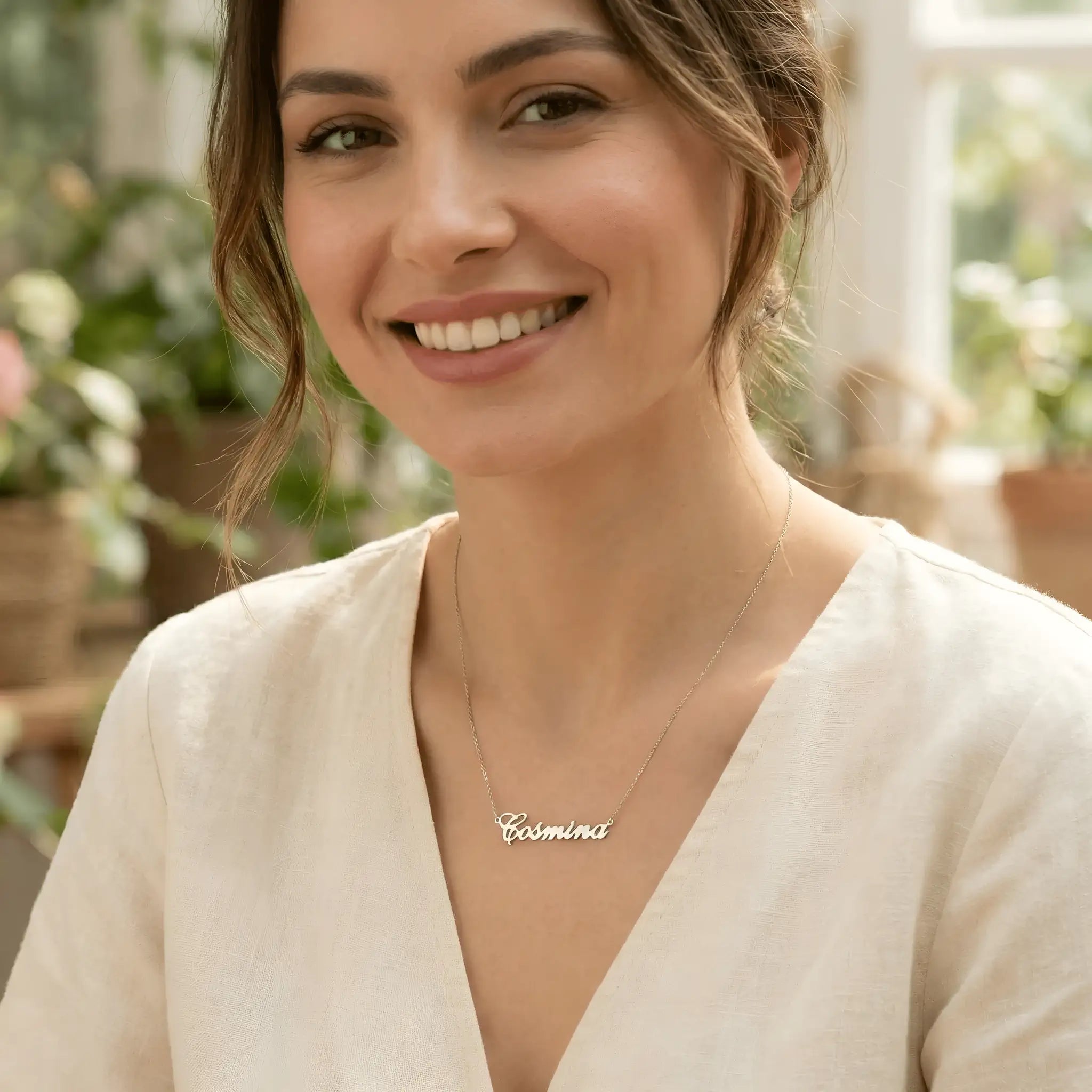 Damă tânără purtând lănțișor argint 925 rodiat cu numele Cosmina script, peste bluză albă de in cu decolteu V, lumină naturală interior cu plante